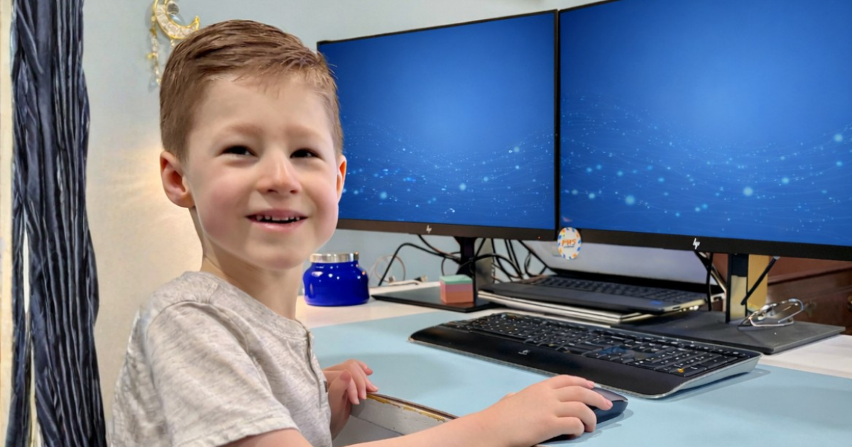 Young boy smiling while using a computer at a desk.