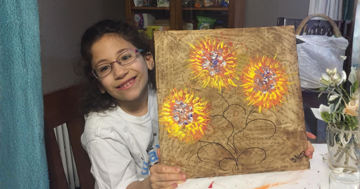 Young girl smiling while holding her original sunflower artwork.