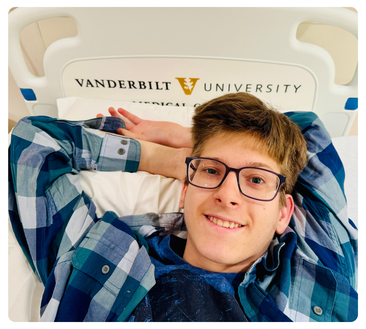 Young man wearing glasses smiling while lying on a hospital bed at Vanderbilt University.