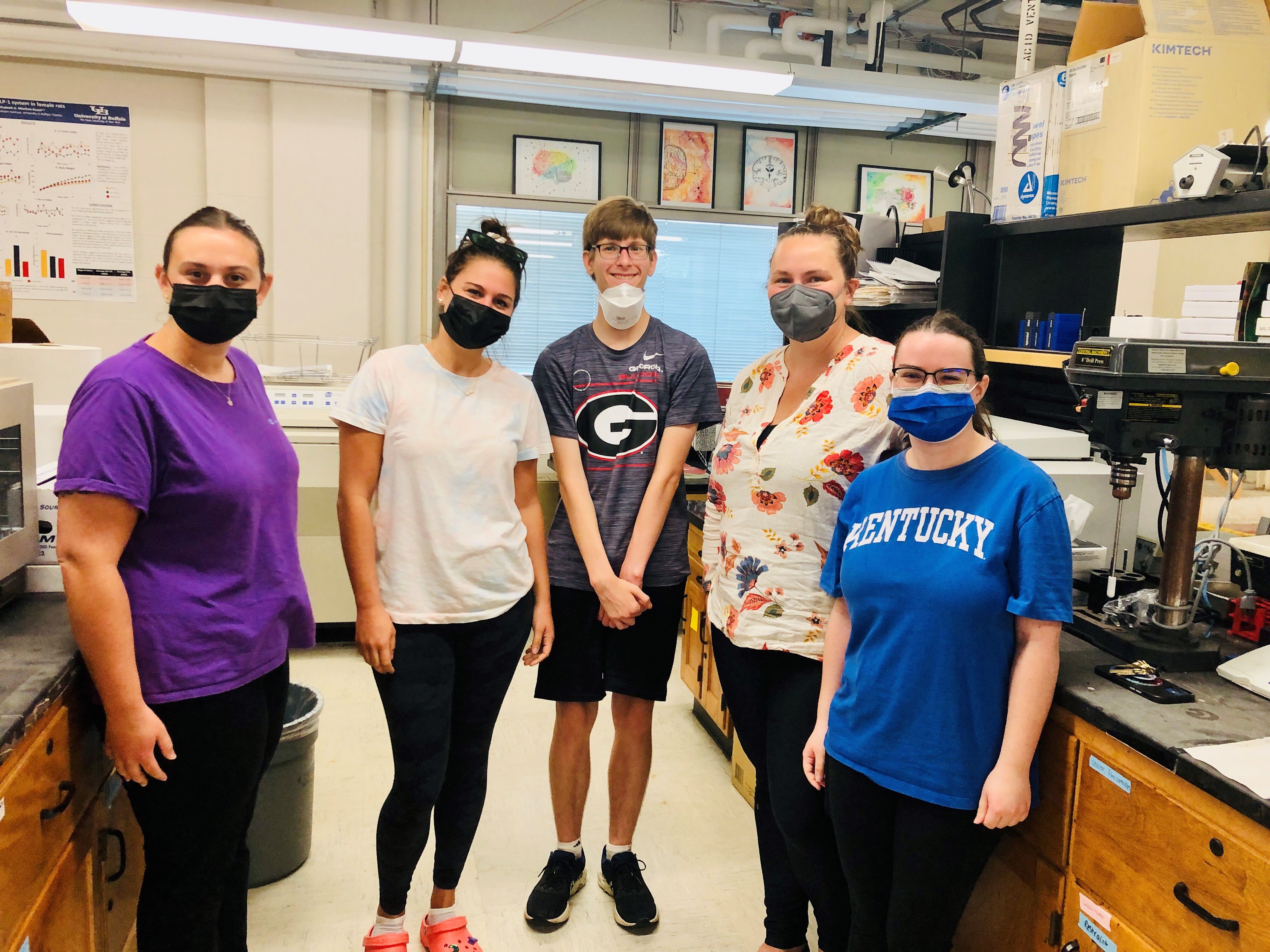 Five people standing together in a research laboratory, several wearing face masks.