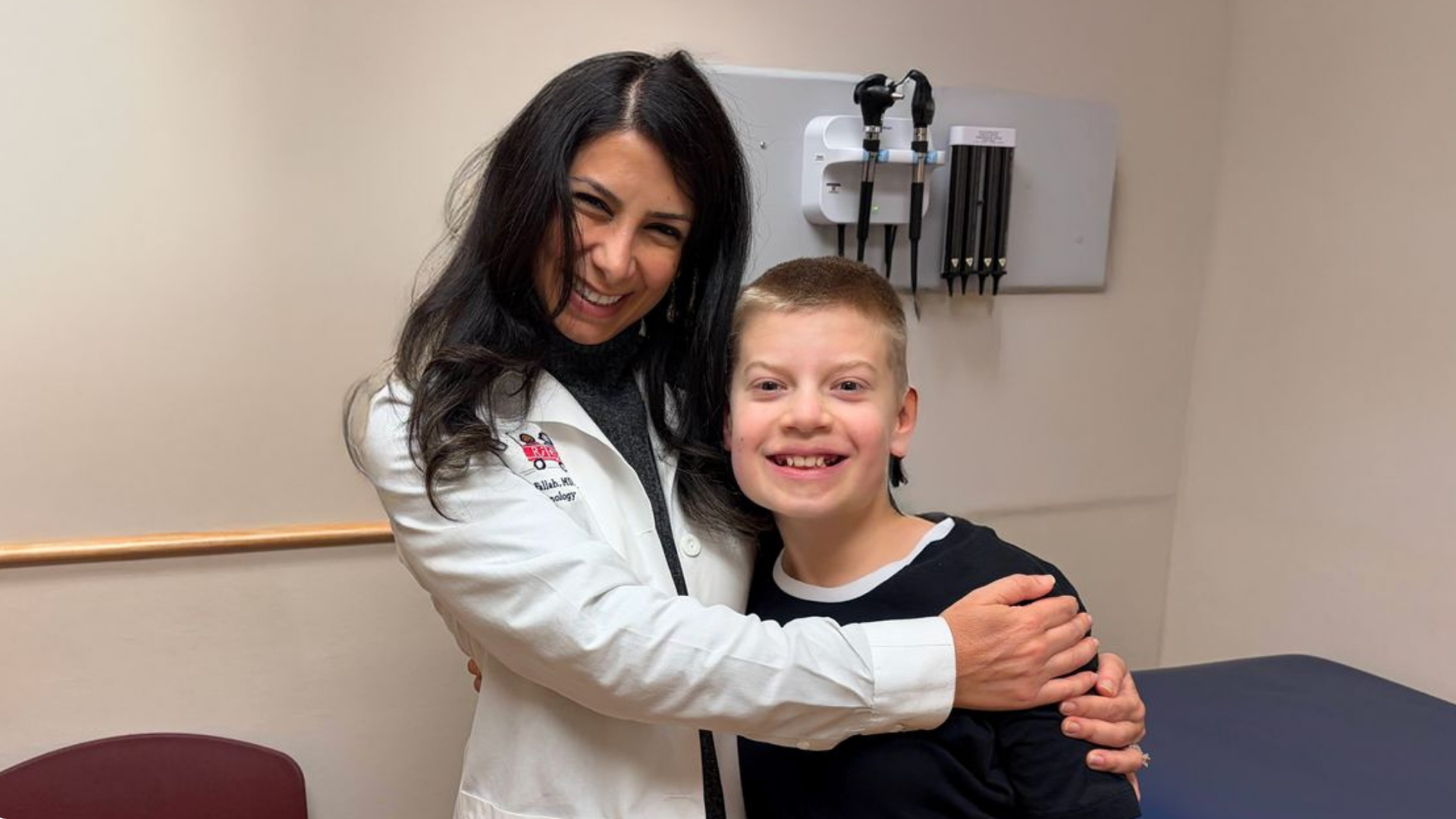 Healthcare professional in a white coat smiling with a young boy during a clinical visit.