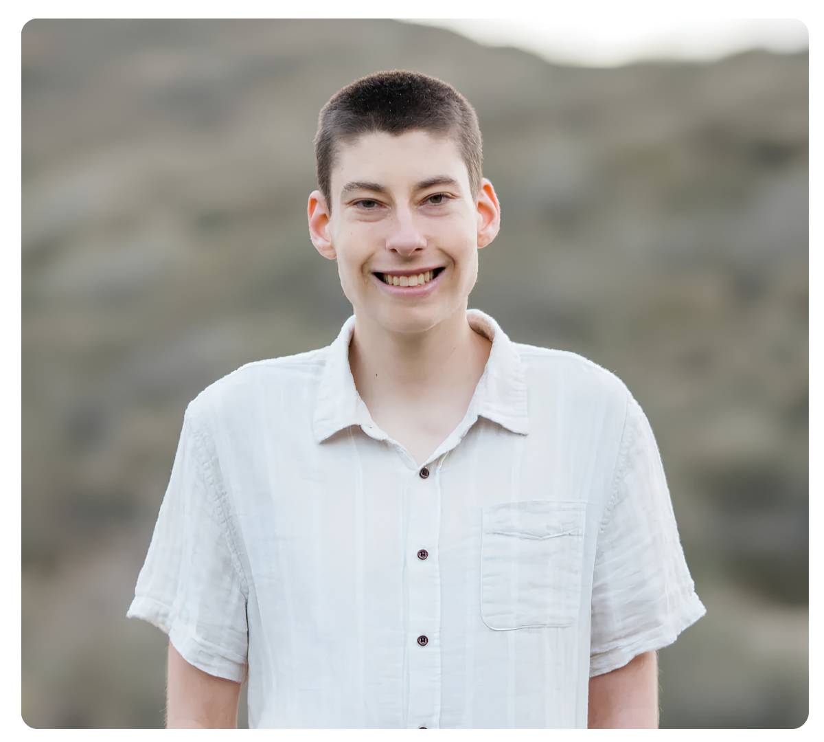 Teen boy smiling outdoors in a white shirt.