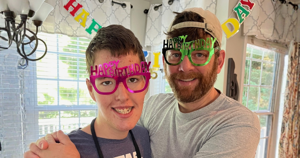 Young man and adult man smiling together while wearing Happy Birthday glasses.