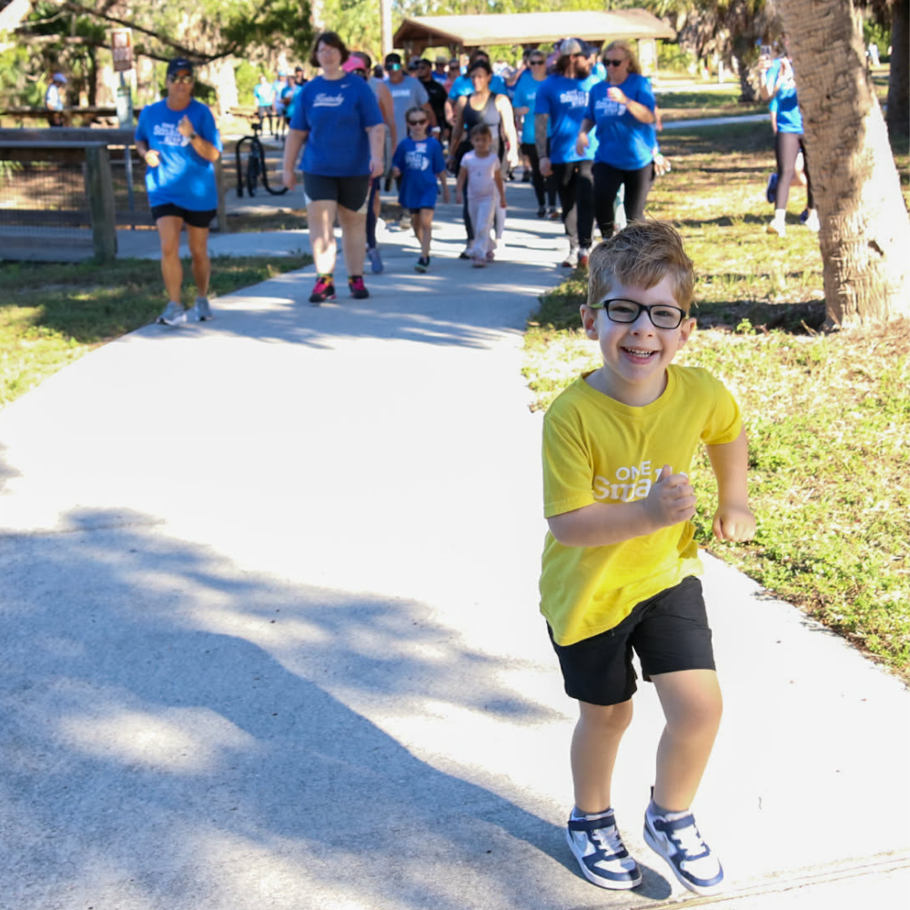 Young boy smiling as he runs ahead of participants at a One Small Step community walk.