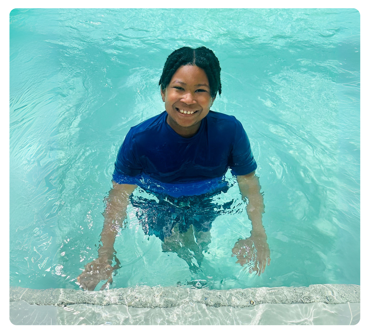 Smiling young man with dark hair standing in a swimming pool.