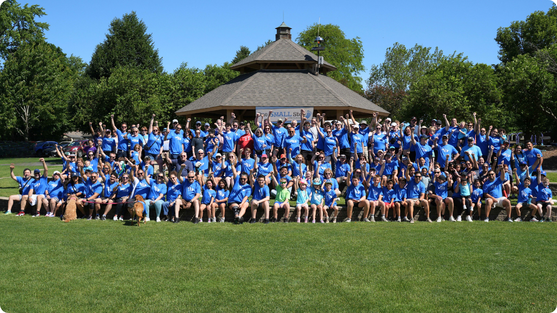 Large group of One Small Step attendees posing together outdoors on a grassy lawn.
