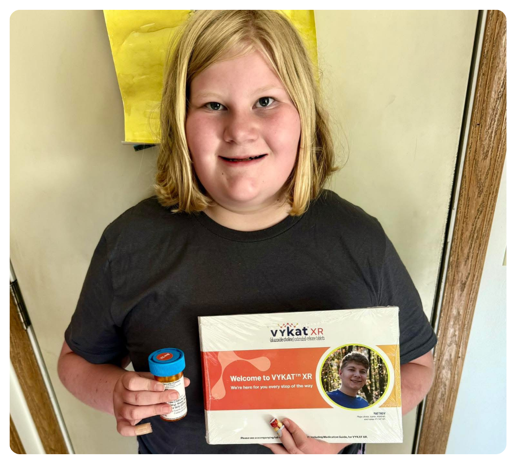Smiling child holding a prescription bottle and VYKAT XR welcome package.