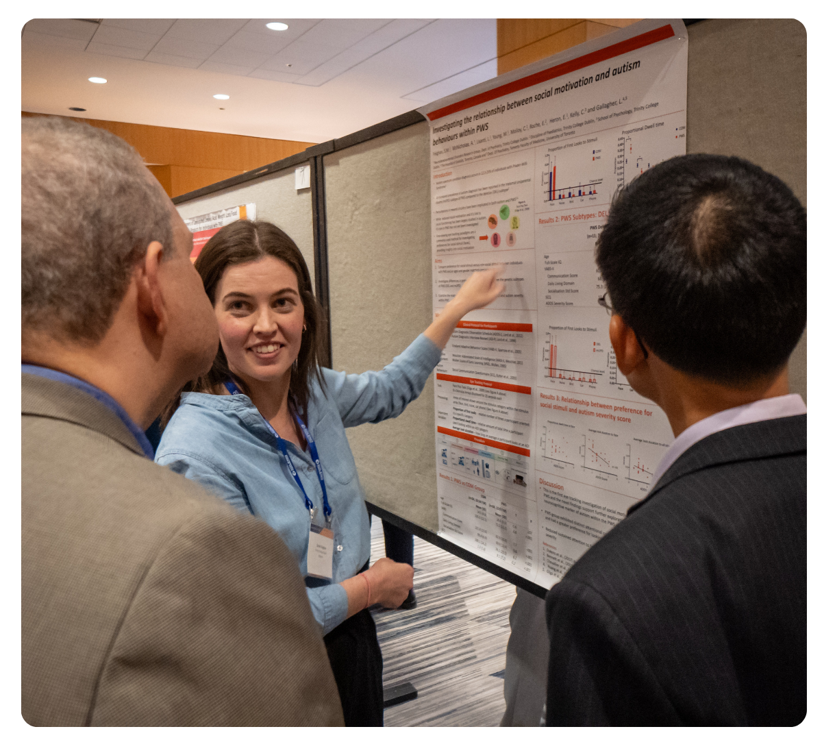 Researcher points to a scientific poster while discussing findings with two conference attendees.
