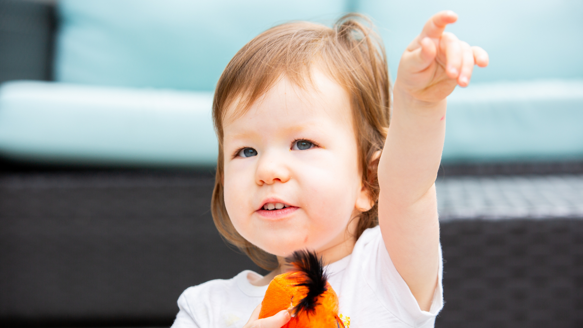 Young child in a white shirt raises one arm while holding an orange-and-black plush toy.
