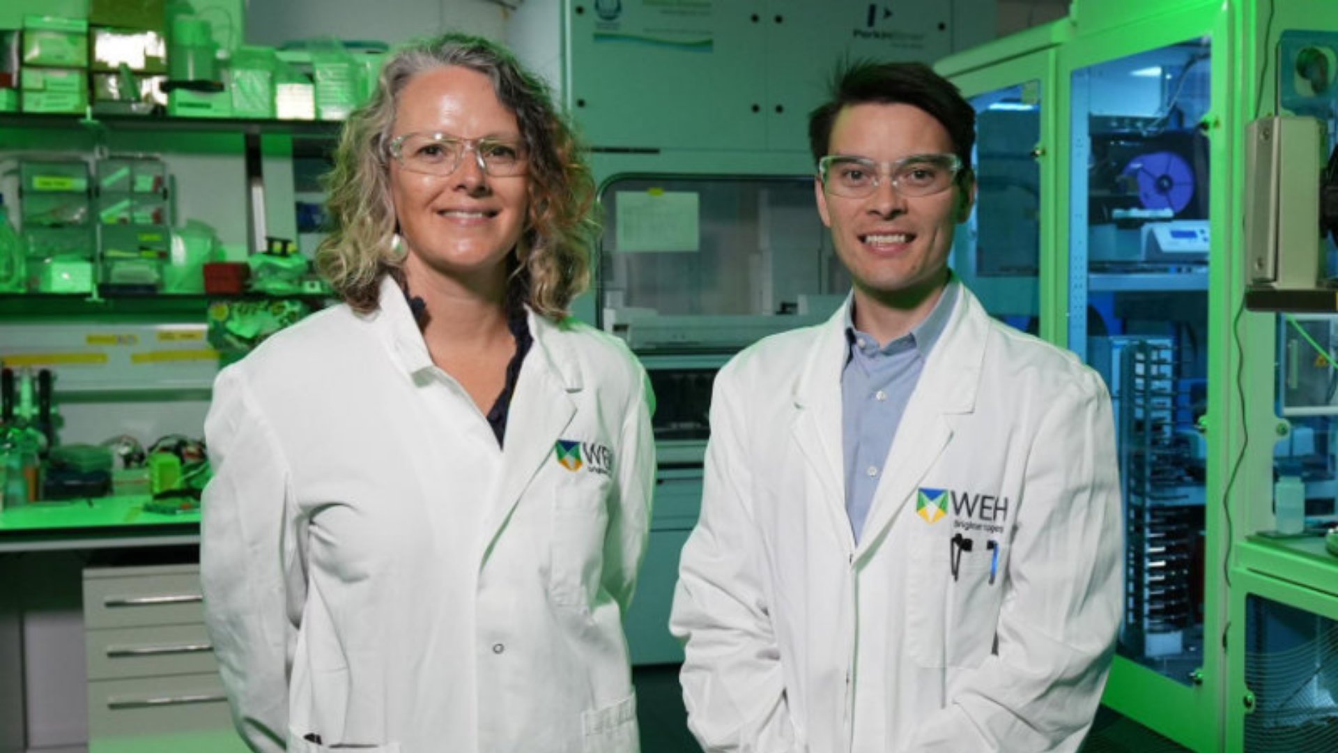 Two researchers wearing lab coats standing together in a laboratory.